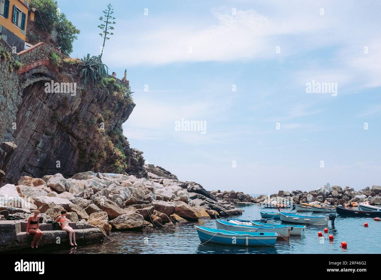 Cinque Terre, Italie - quai à Riomaggiore avec des bateaux et des touristes en maillots de bain. Ville balnéaire sur la Riviera italienne. Les gens sur une plage rocheuse sous le soleil Banque D'Images