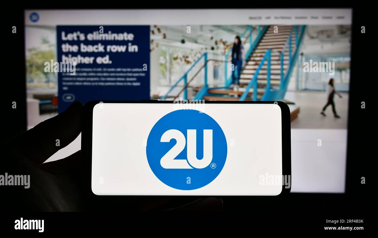 Personne détenant un smartphone avec le logo de la société de technologie éducative américaine 2U Inc. Sur l'écran devant le site Web. Concentrez-vous sur l'affichage du téléphone. Banque D'Images