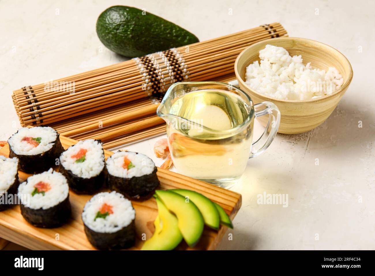 Plateau en bois avec de savoureux petits pains à sushis, des ingrédients, un tapis de bambou et des baguettes sur fond clair Banque D'Images