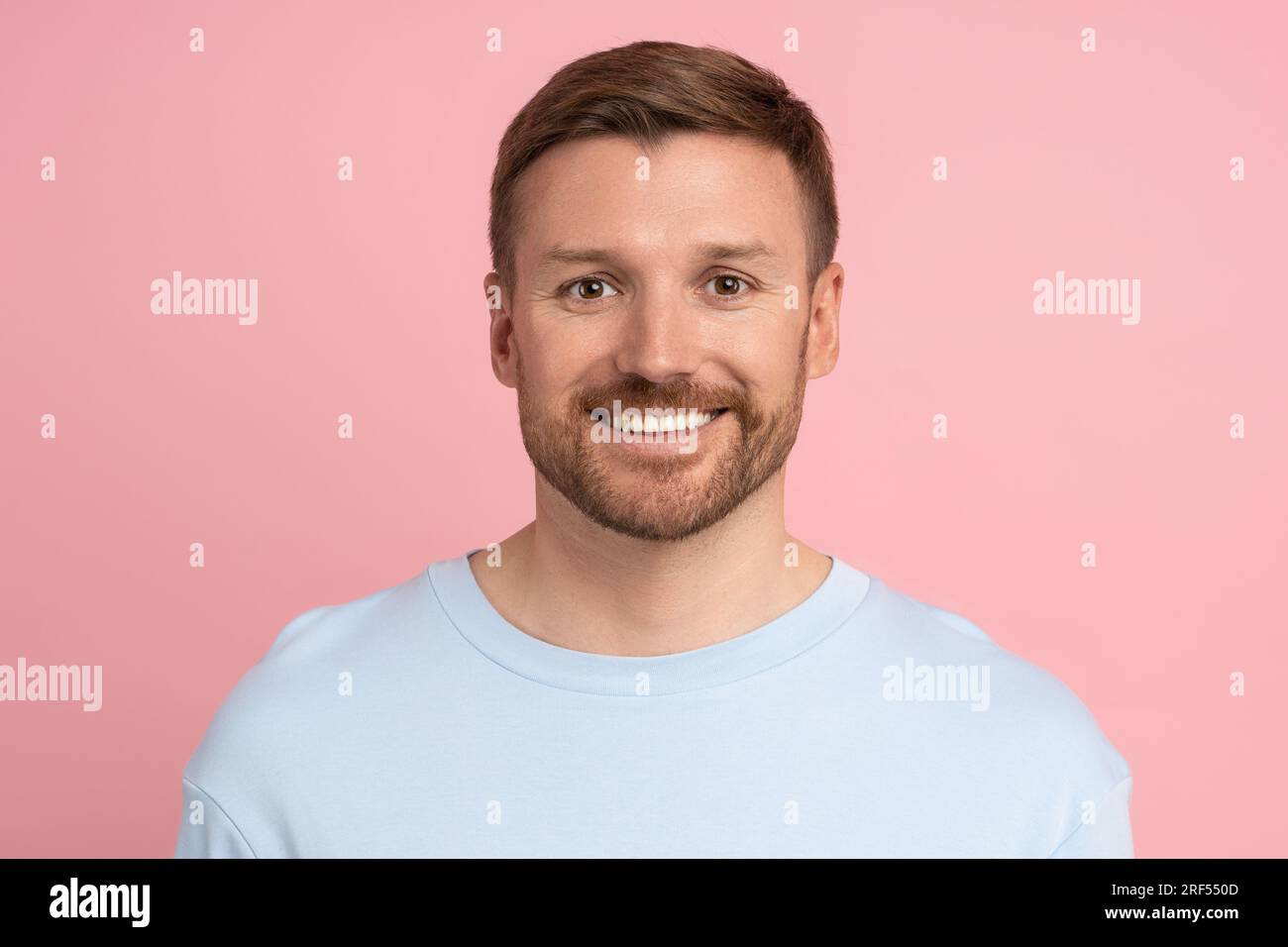 Portrait de caucasien barbu bel homme regardant la caméra souriant sur fond de studio rose. Banque D'Images