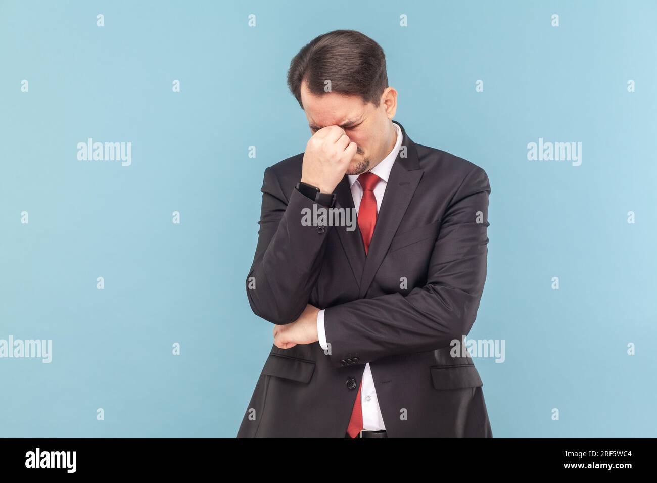 Portrait de triste homme bouleversé pleurant avec la moustache debout la tête en bas, entendant de très mauvaises nouvelles, portant un costume noir avec une cravate rouge. Prise de vue en studio d'intérieur isolée sur fond bleu clair. Banque D'Images