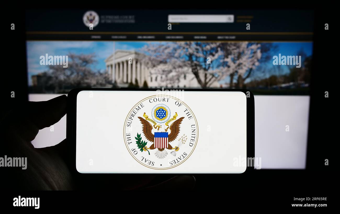 Personne tenant un téléphone portable avec le sceau des États-Unis Cour suprême (SCOTUS) à l'écran devant la page Web. Concentrez-vous sur l'affichage du téléphone. Banque D'Images