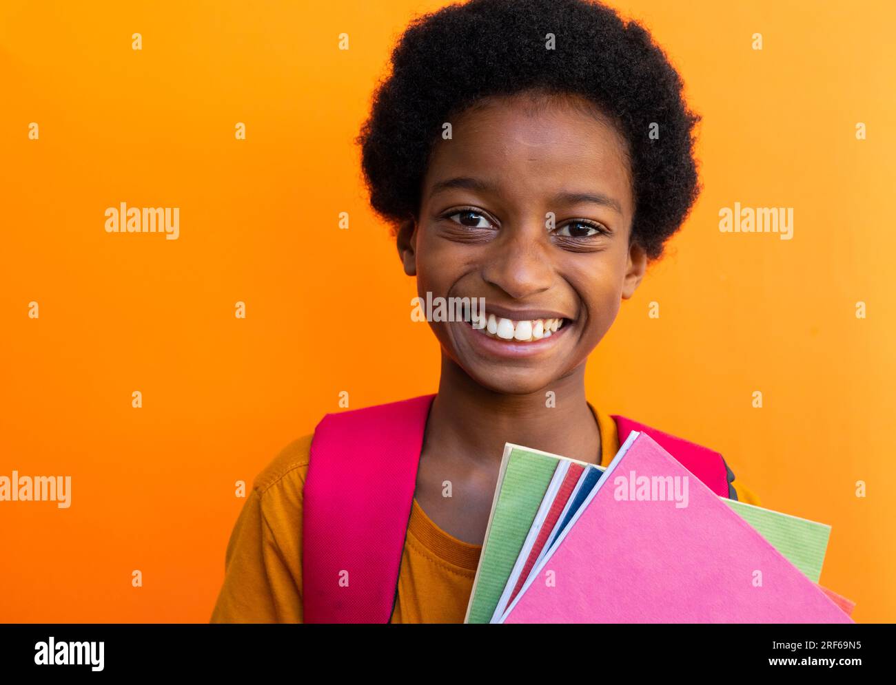 Portrait d'écolier biracial heureux avec des livres portant un tshirt jaune sur fond orange Banque D'Images