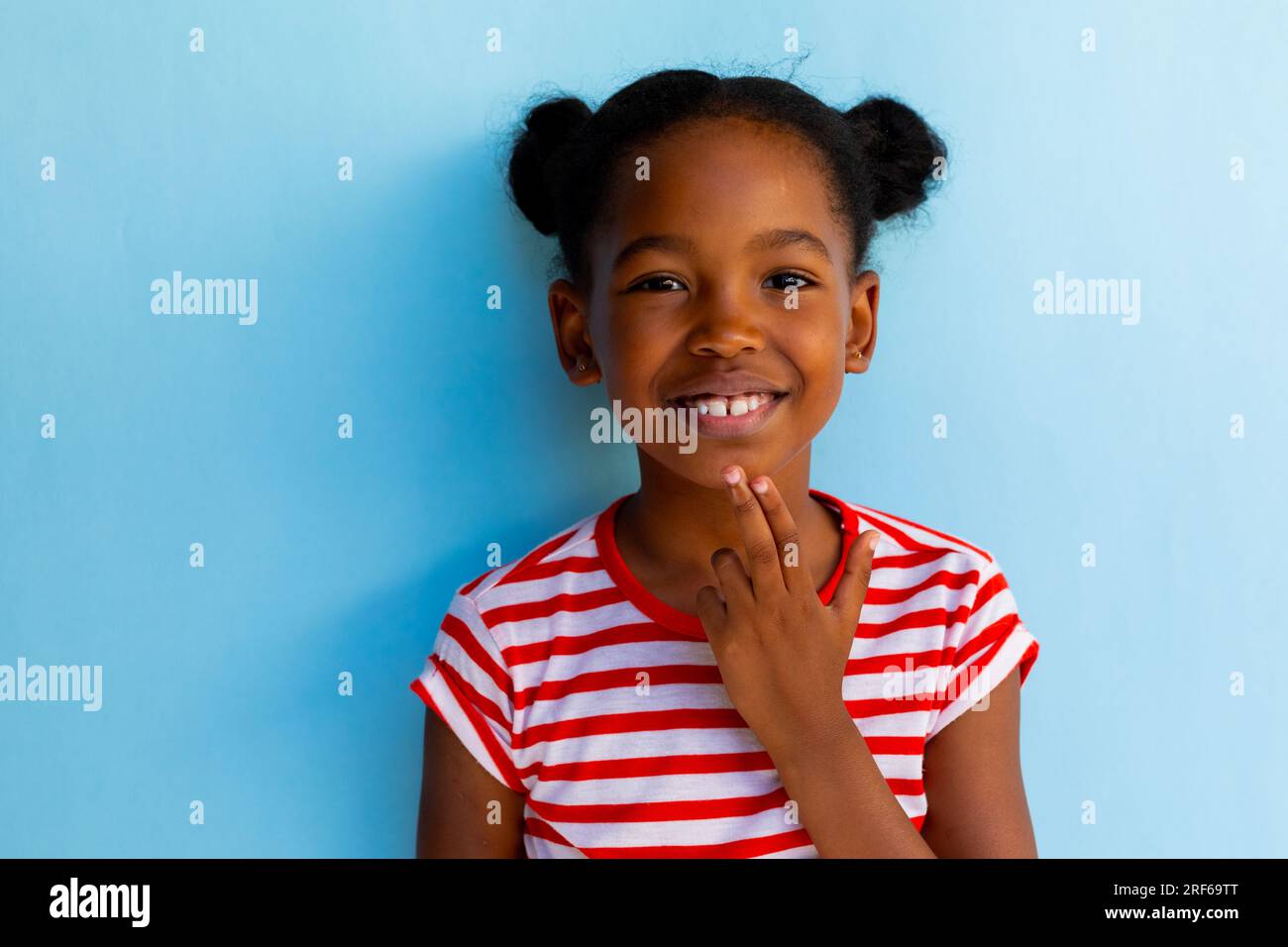 Heureuse écolière afro-américaine faisant la langue des signes avec la main sur fond bleu Banque D'Images
