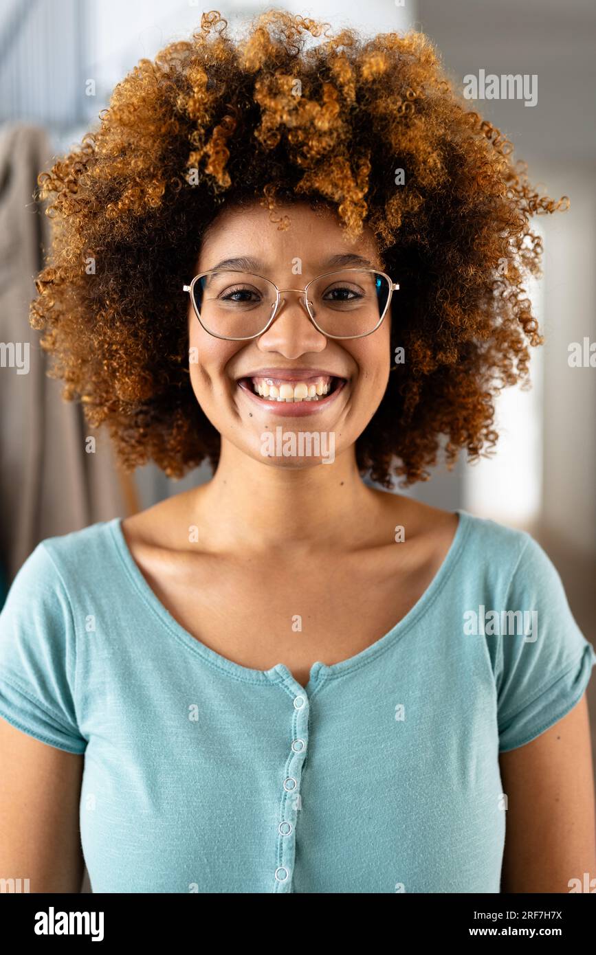 Portrait de femme biracial heureuse avec les cheveux bouclés et les lunettes à la maison Banque D'Images