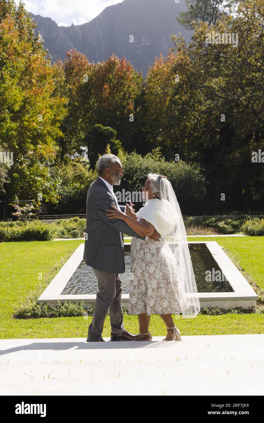 Heureux senior biracial mariée et marié dansant dans le jardin à la cérémonie de mariage ensoleillée, espace de copie Banque D'Images