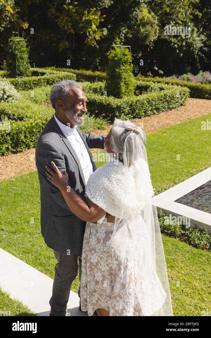 Heureux senior biracial mariée et marié dansant dans le jardin à la cérémonie de mariage ensoleillée, espace de copie Banque D'Images