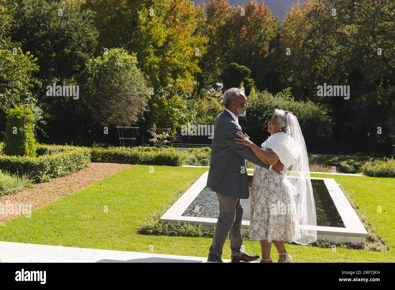 Heureux senior biracial mariée et marié dansant dans le jardin à la cérémonie de mariage ensoleillée, espace de copie Banque D'Images