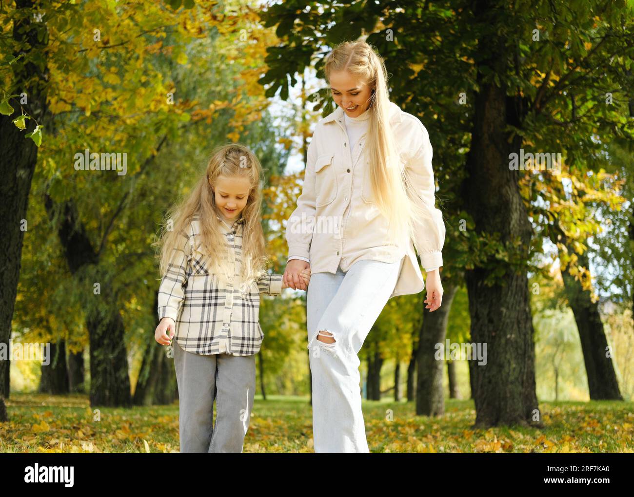 Famille passer du temps ensemble dans le parc d'automne. Mère et fille marchent dans le parc d'automne et jettent des feuilles avec leurs pieds. Photo horizontale Banque D'Images