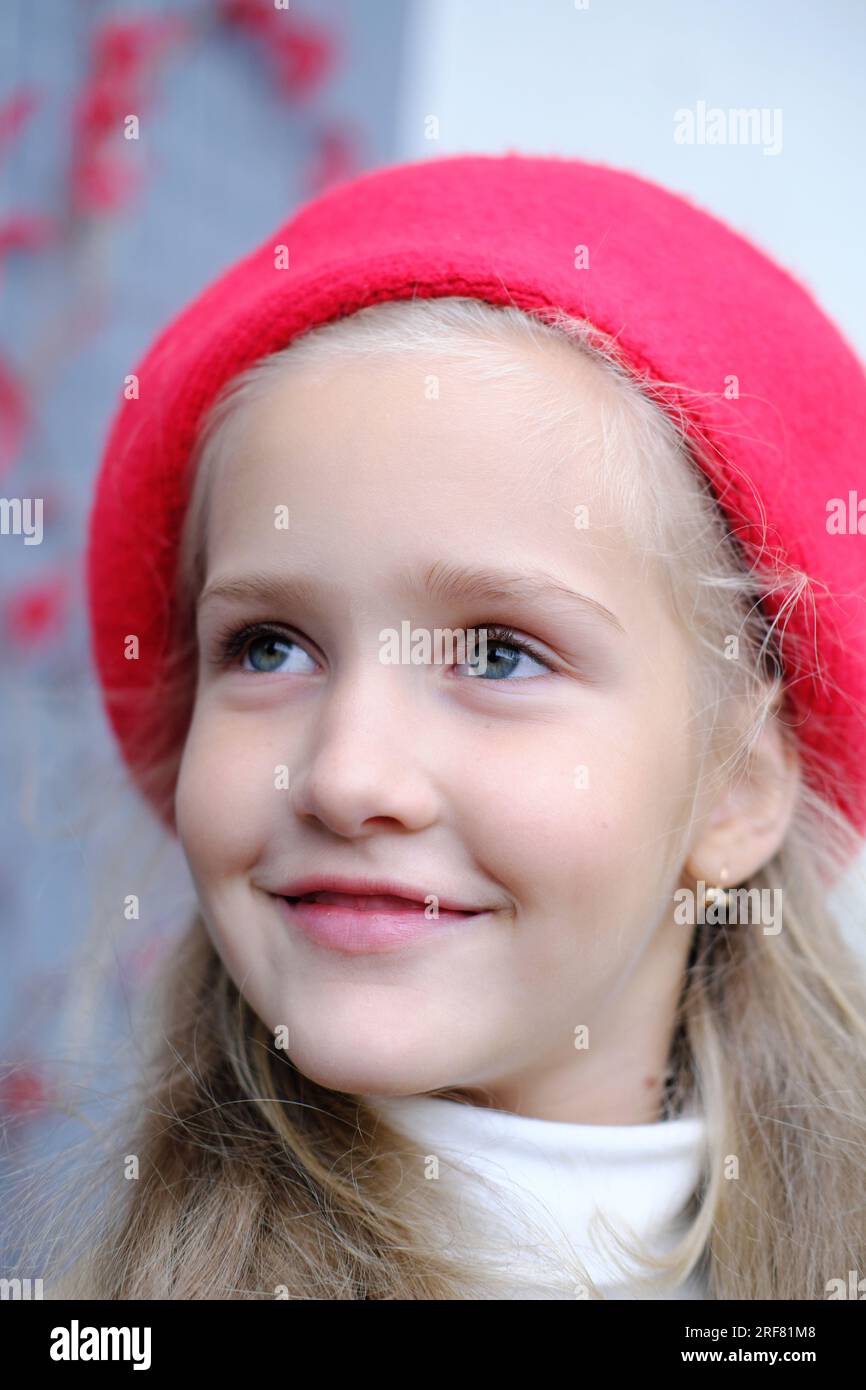 Portrait d'une belle petite fille dans un trench coat et un béret rouge. Une fille pose alors qu'elle est assise à une table dans un café de la rue. Photo verticale Banque D'Images