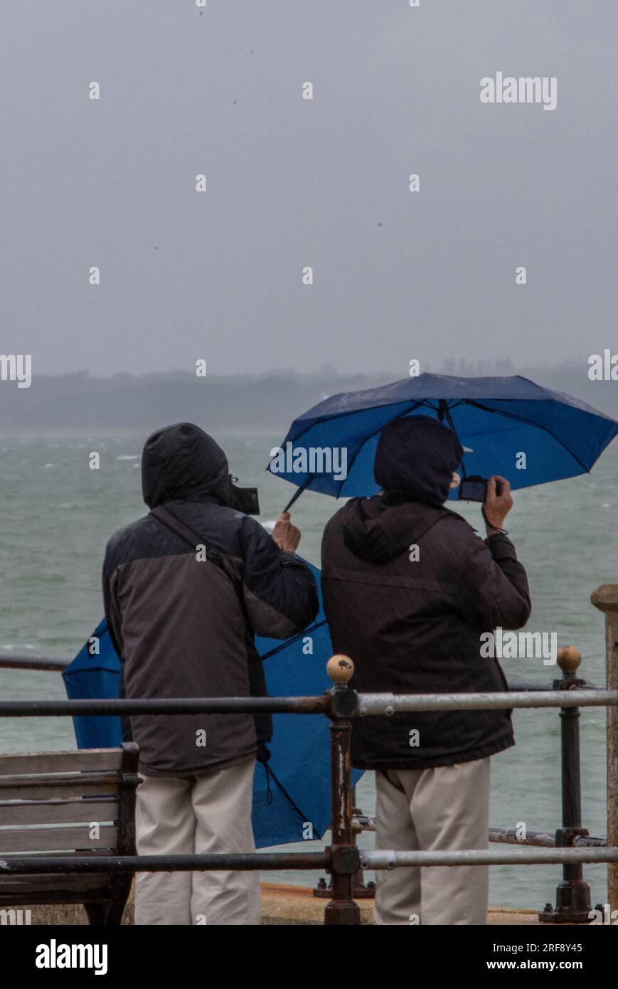 famille debout sous la pluie avec des parapluies au bord de la mer. famille en vacances sous la pluie battante utilisant des parapluies pour se protéger et rester au sec. Banque D'Images