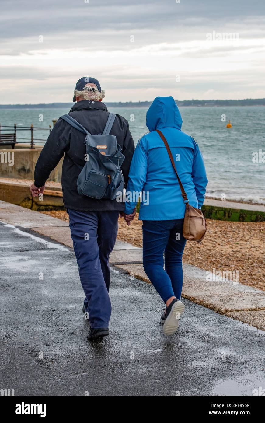 couple marchant ensemble dans la pluie battante sur une journée humide au bord de la mer. homme et femme portant des vestes imperméables à marcher dans une averse. Banque D'Images