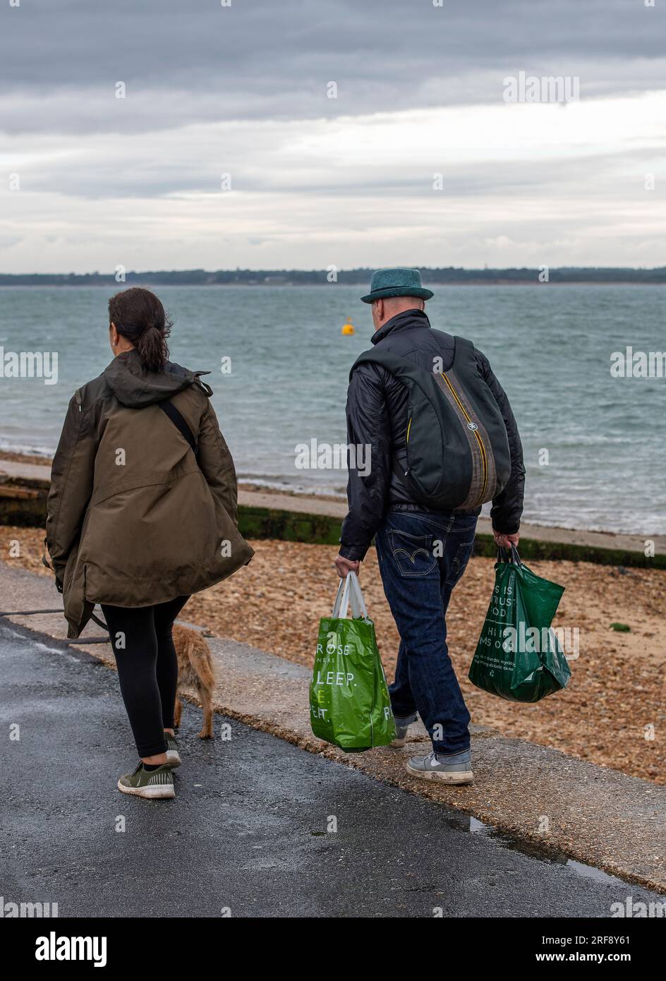 couple plus âgé transportant des magasins à la maison le long d'un sentier de bord de mer par une journée humide orageuse. Banque D'Images