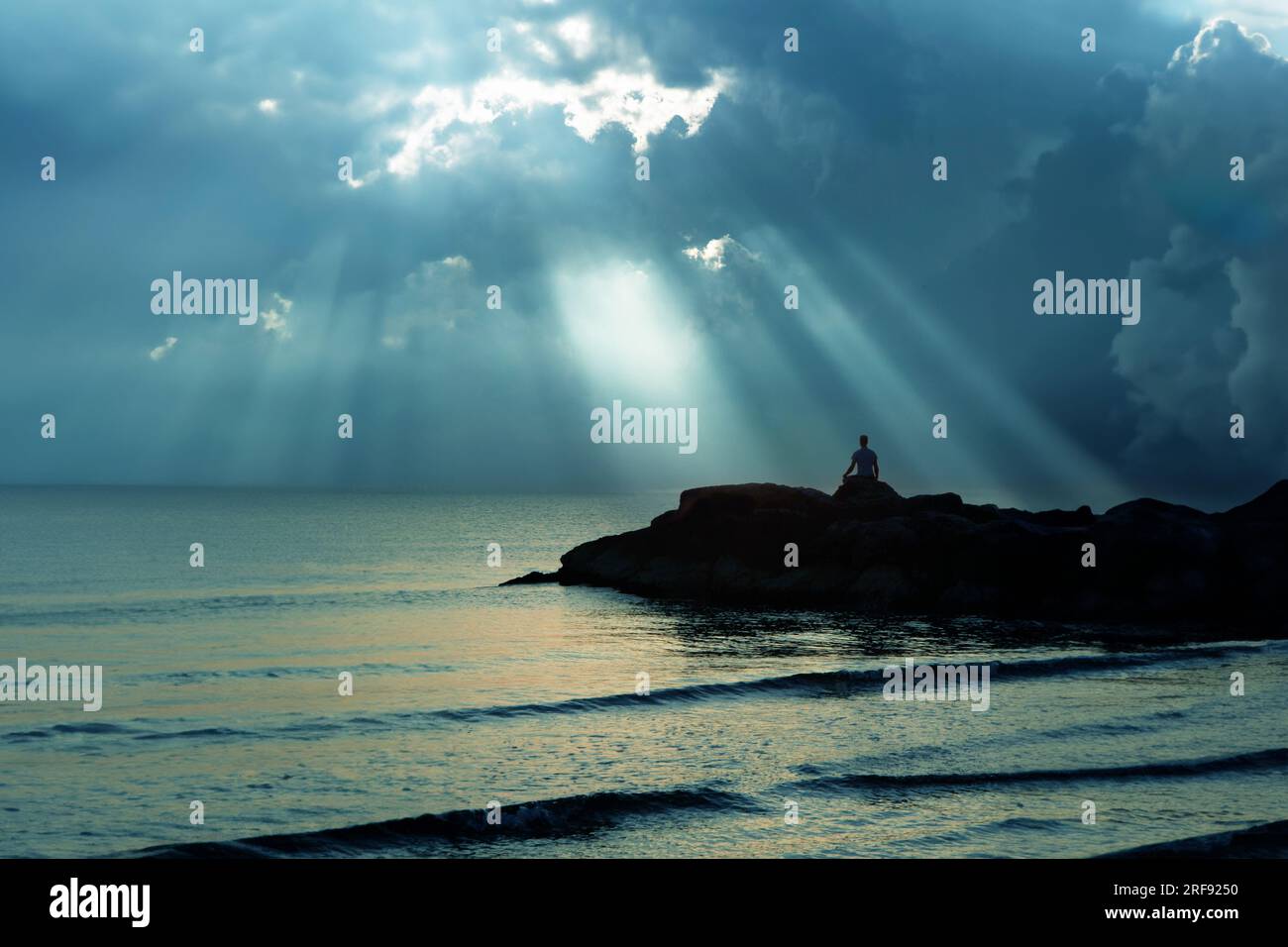 Vue nocturne sur la mer avec homme pratiquant le yoga sur les rochers Banque D'Images