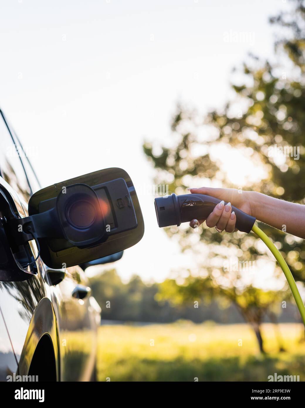 Jeune femme brancher le chargeur dans une voiture électrique noire, concept d'énergie renouvelable Banque D'Images