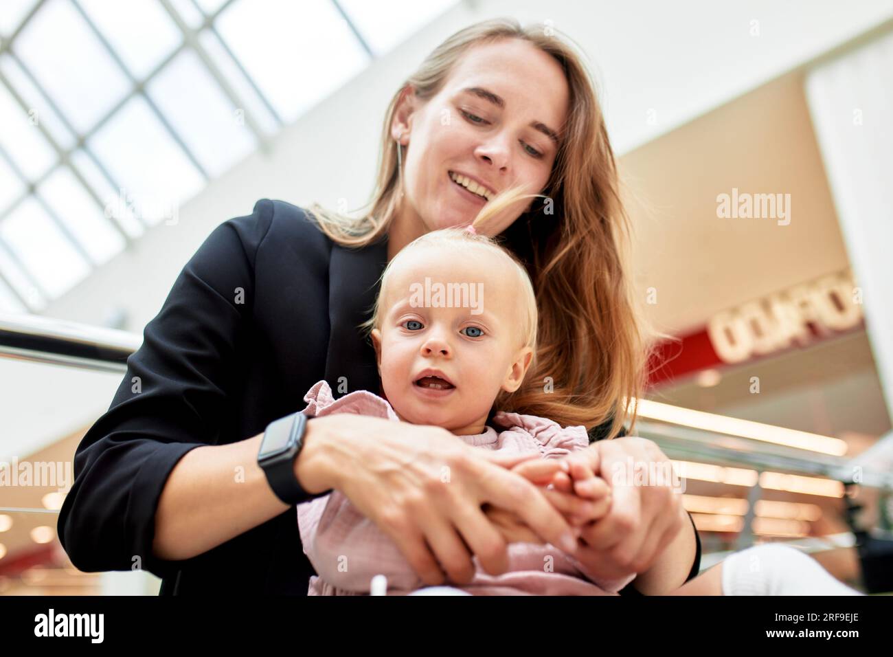 Jeune jolie mère avec un petit bébé assis sur un banc dans un centre commercial. Maman et fille dans les vêtements roses câliner, jouer, se détendre et s'amuser tout en sh Banque D'Images
