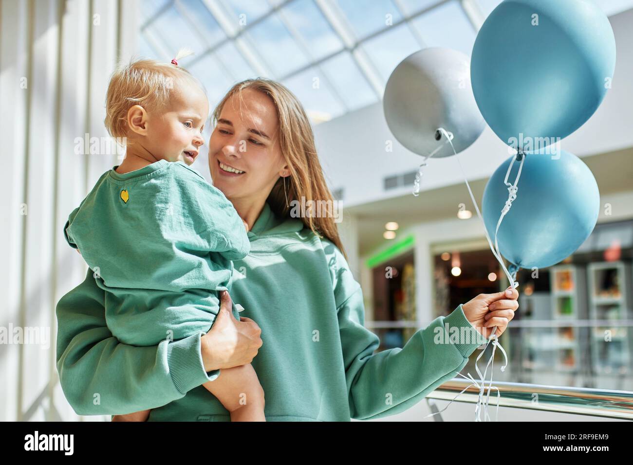 Portrait de mère heureuse avec bébé dans ses bras et ballons colorés. Jeune jolie maman et sa petite fille dans les mêmes vêtements verts marchent autour de la maman Banque D'Images