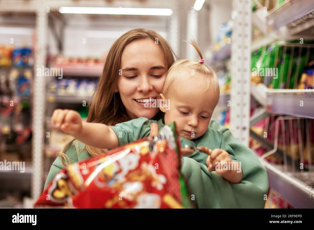 Heureuse jeune mère avec sa fille mignonne marchant autour d'un supermarché avec chariot. Maman et petite fille blonde choisissant des marchandises et ayant Banque D'Images
