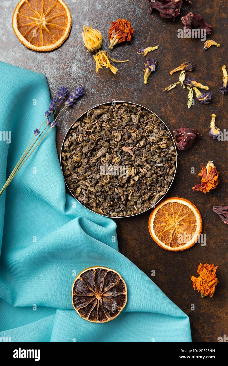 Composition de tranches de vert, de thé floral et d'orange séchée sur fond bleu et marron vue du dessus. Thé à grandes feuilles, fleurs séchées et chips d'agrumes Banque D'Images