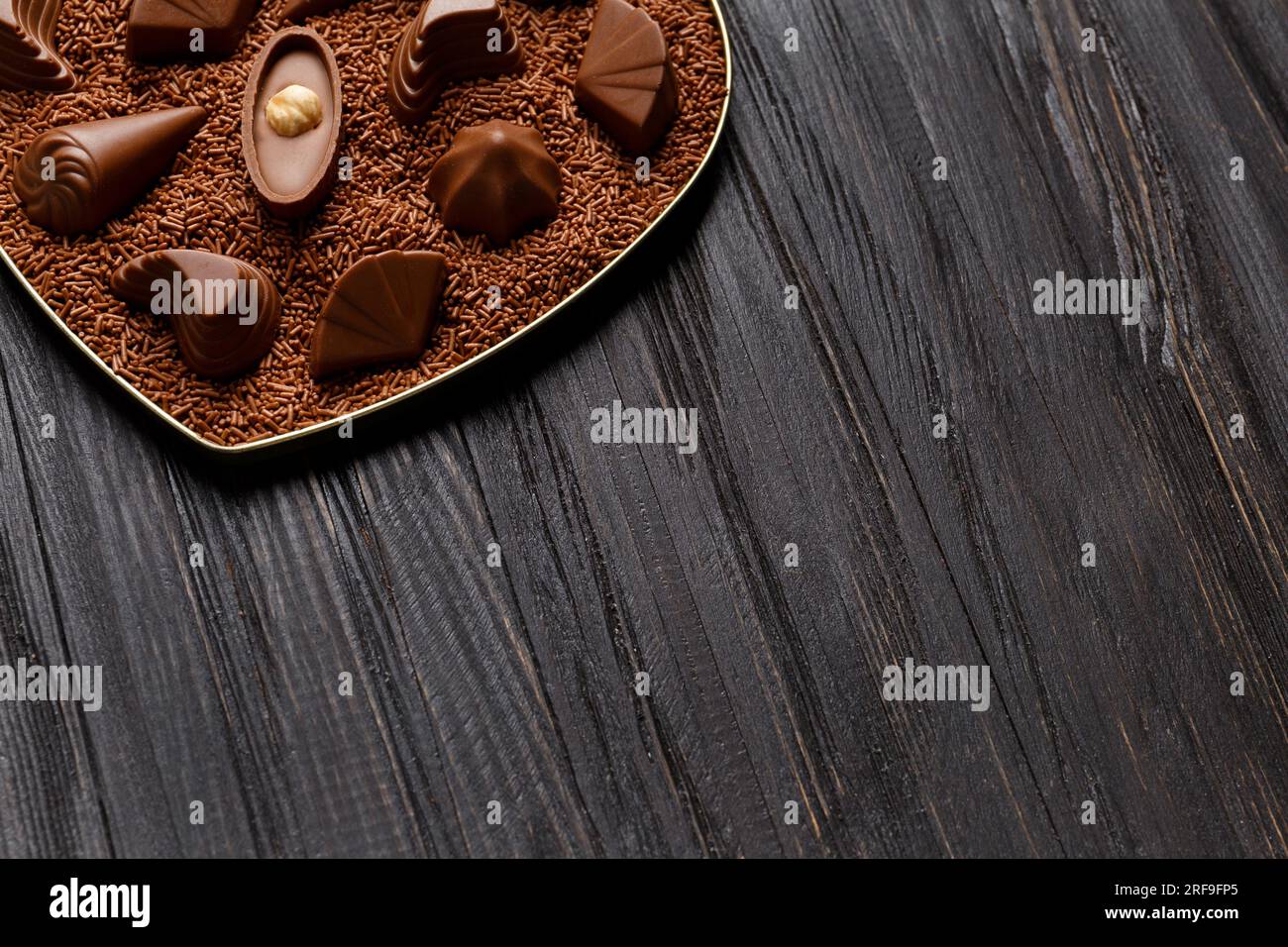 Bonbons au chocolat se trouvent dans des pépites de chocolat dans une boîte sur un fond en bois sombre, gros plan. Mélange de bonbons pralinés au chocolat, espace de copie. Banque D'Images