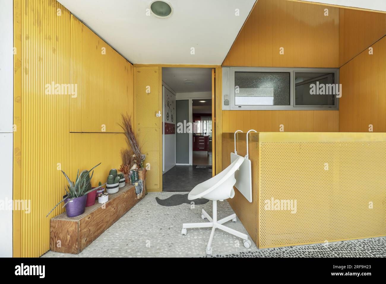 Porche d'entrée d'une maison avec une corde à linge, un banc en bois pour placer les plantes et les murs peints en jaune Banque D'Images