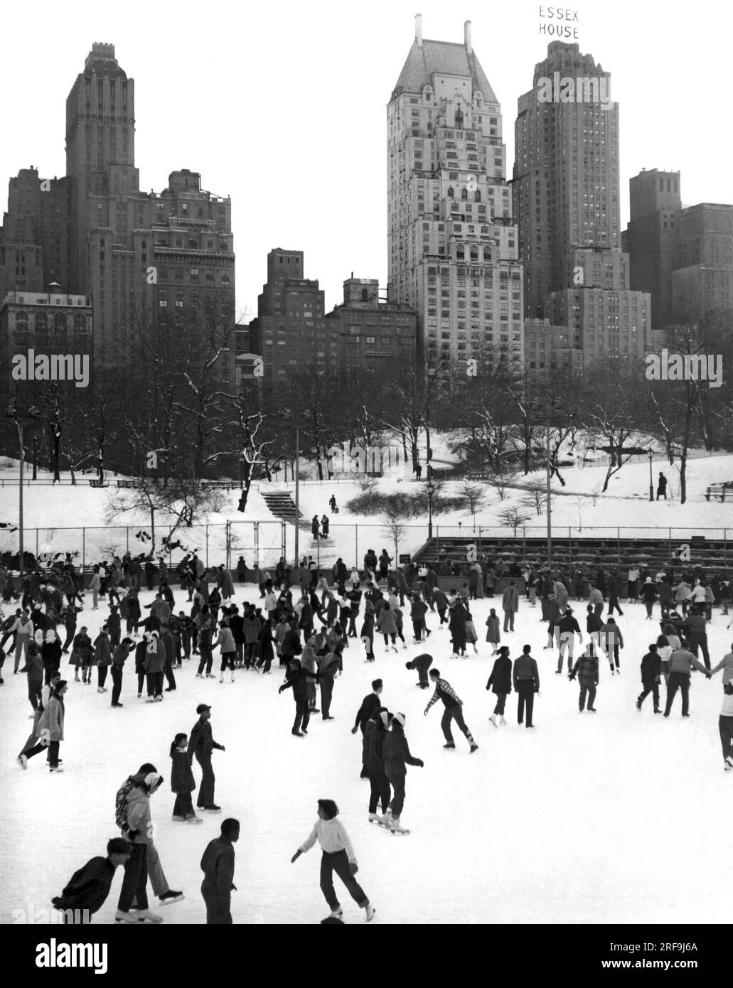 New York, New York : c. 1952 patinage sur glace à Central Park à la patinoire de la 59th Street à New York avec l'Essex House en arrière-plan. Banque D'Images