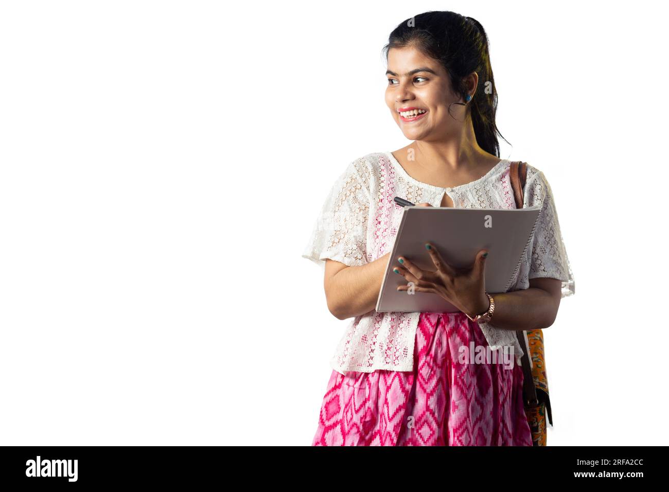 Portrait d'une jeune fille indienne heureuse prenant des notes et regardant latéralement sur fond blanc Banque D'Images