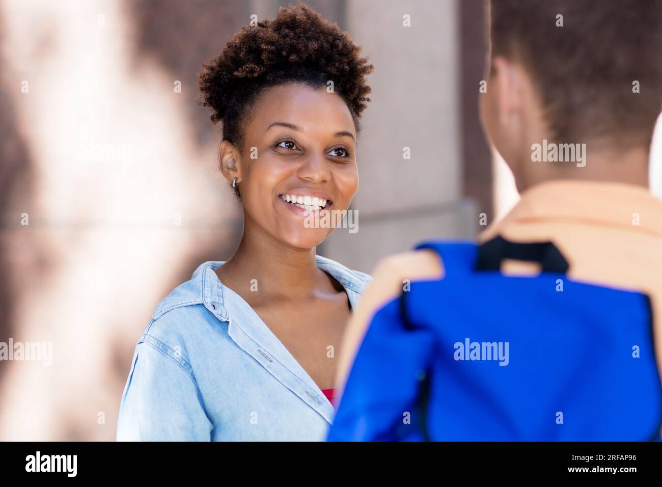 Femme afro-américaine parlant et riant avec un ami en plein air dans la ville en été Banque D'Images