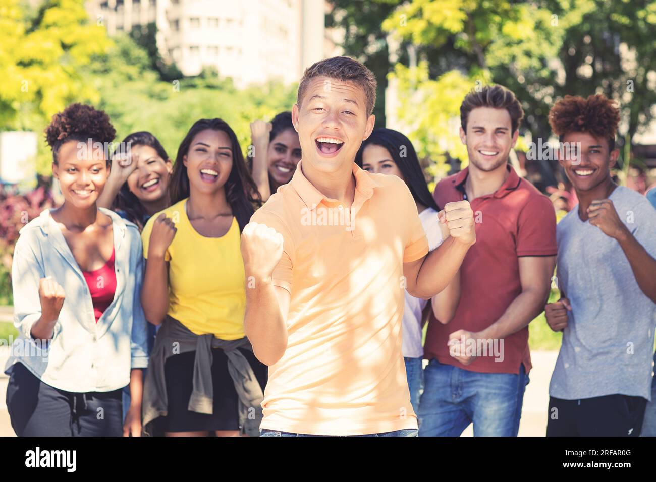 Jeune étudiant masculin avec groupe de jeunes adultes acclamants en plein air en été dans la ville Banque D'Images