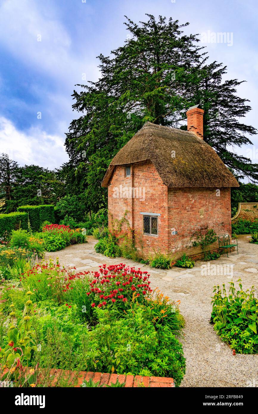 Un petit cottage en briques rouges avec toit de chaume entouré de bordures colorées dans le Cottage Garden à 'The Newt in Somersets', nr Bruton, Angleterre, Royaume-Uni Banque D'Images