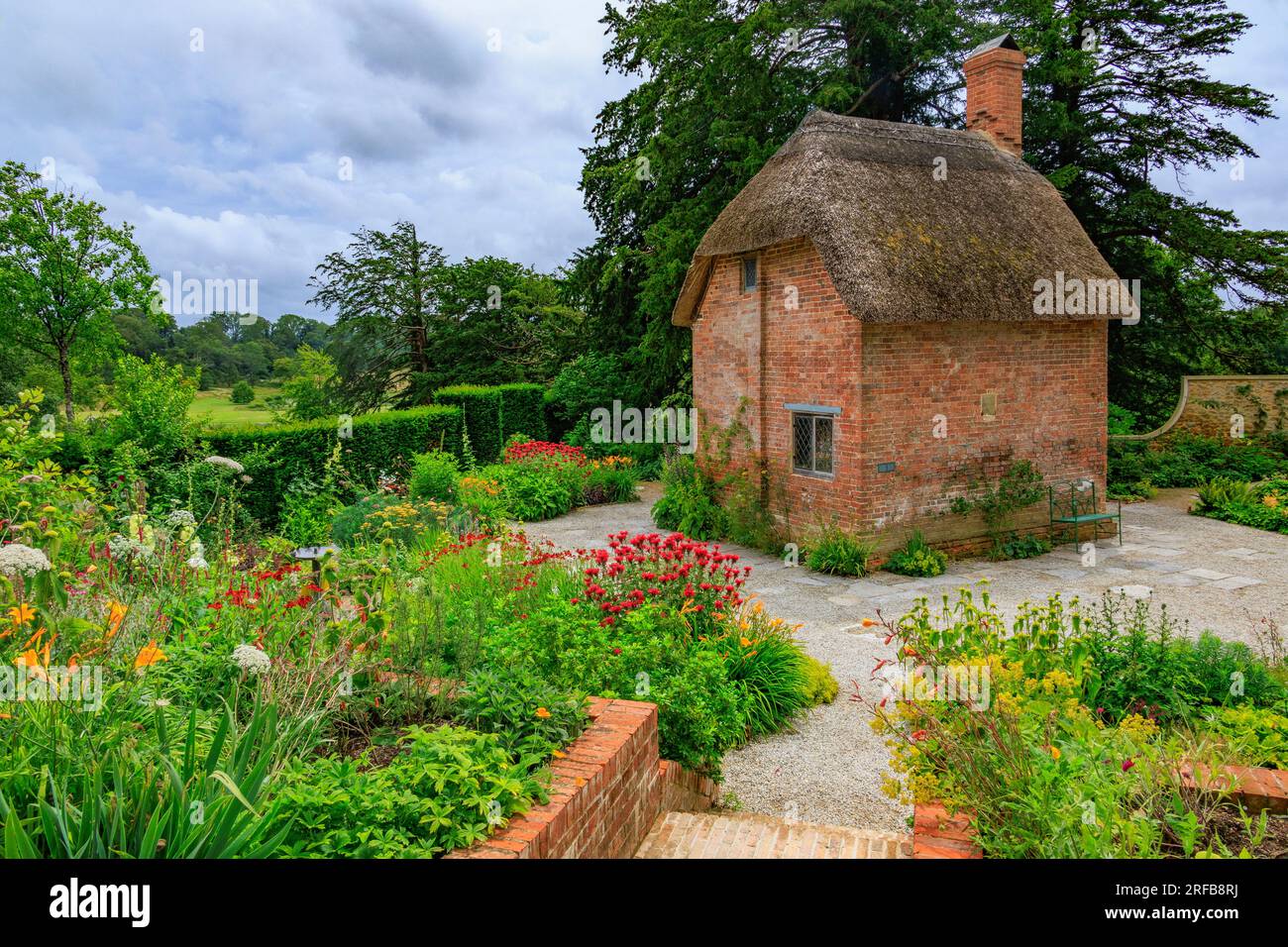 Un petit cottage en briques rouges avec toit de chaume entouré de bordures colorées dans le Cottage Garden à 'The Newt in Somersets', nr Bruton, Angleterre, Royaume-Uni Banque D'Images