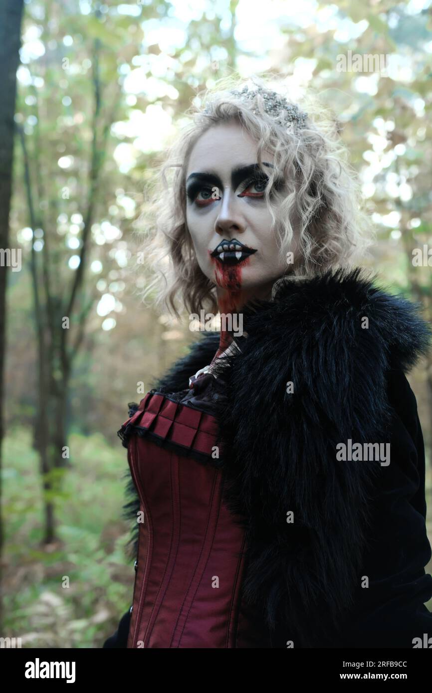 Une femme en forme de vampire ou de sorcière en robe médiévale marche dans la forêt. Vampire à la recherche d'une victime. Photo verticale Banque D'Images