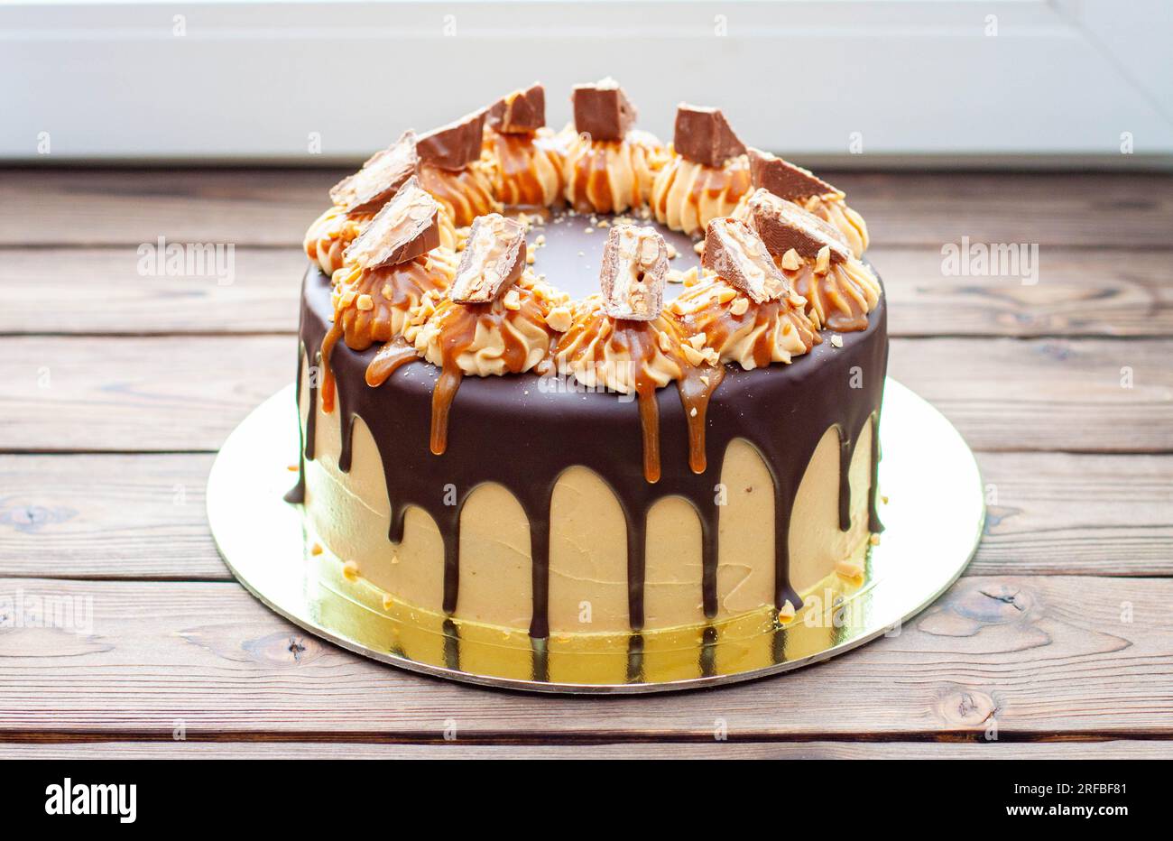 Gâteau à la crème au beurre de cacahuète avec chocolat fondu, barres de bonbons, bouchées de cacahuètes et caramel salé sur fond de bois Banque D'Images