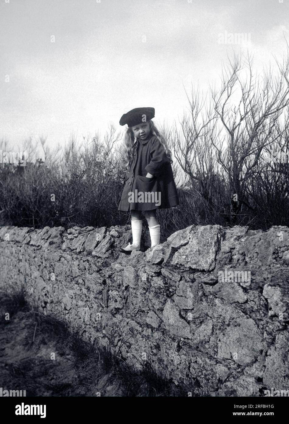 Elegante petite fille posant debout sur un muret de pierre. Bretagne (France), photographie 1917. Banque D'Images