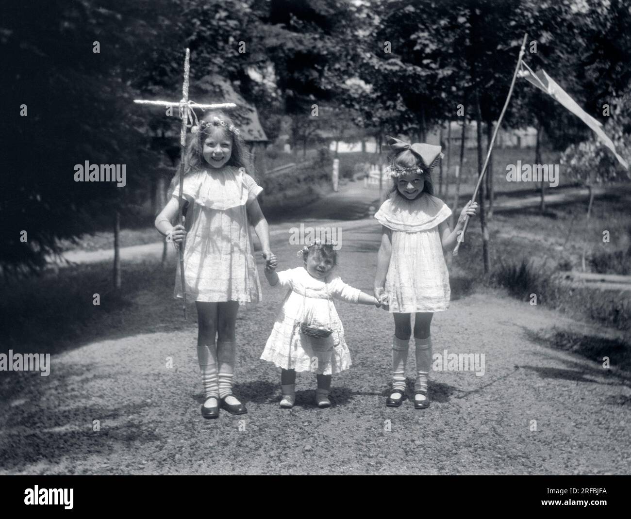 Trois petites filles, en robes de dentelle, portant croix, panier et fanion pour une procession. Bretagne (France), photographie 1921-1922. Banque D'Images