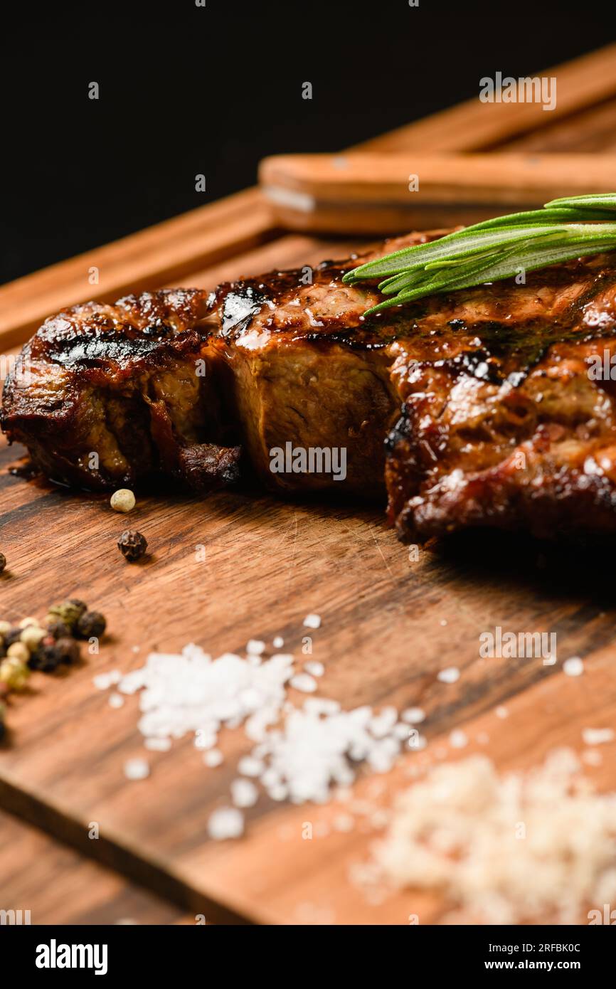 Steak juteux appétissant sur une planche à découper en bois. Gros plan, vue de dessus. Arrière-plan sombre. Banque D'Images