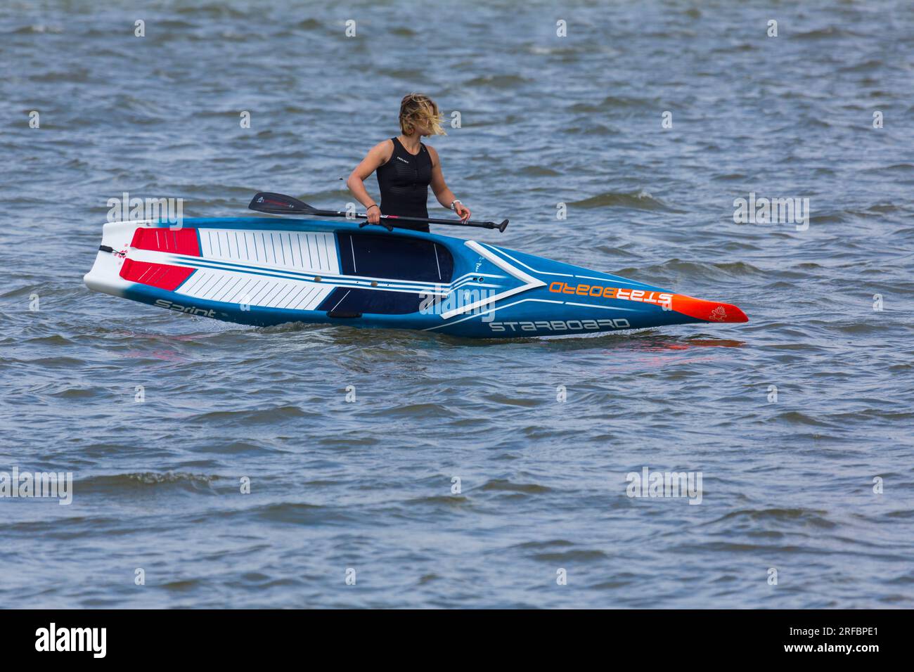 Femme portant une combinaison sans manches Prolimit portant Starboard Sprint paddleboard en mer à Sandbanks, Poole, Dorset UK en juillet Banque D'Images