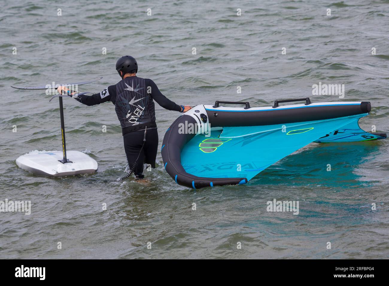Homme portant la combinaison O'Neill portant l'aile wingfoil dans la mer prêt à aller aile foil wingfoiling à Sandbanks, Poole, Dorset Royaume-Uni en juillet Banque D'Images