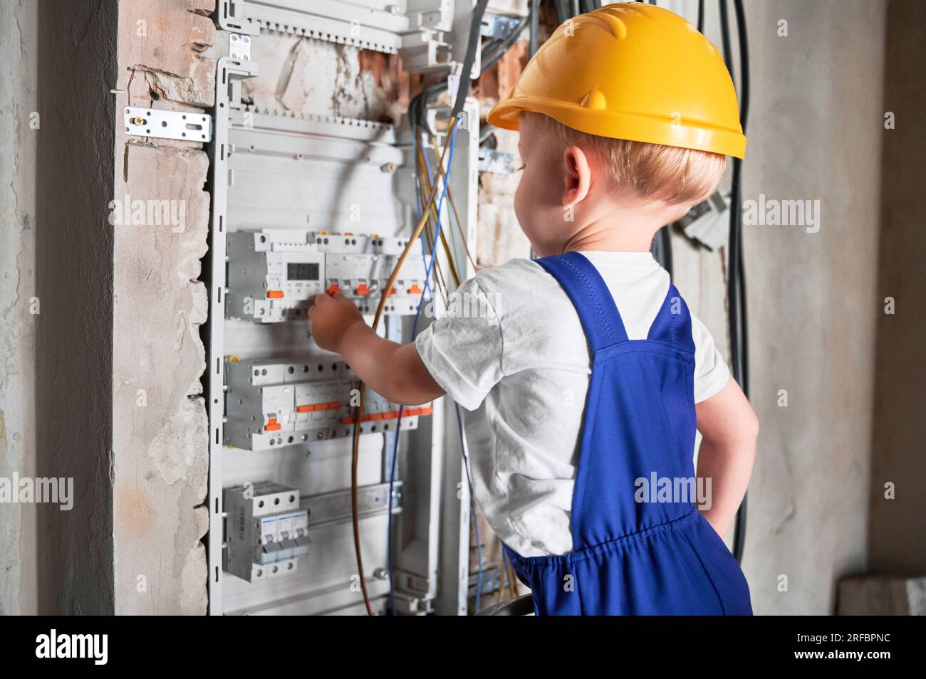 Vue latérale du tableau de distribution ou de commutation électrique de fixation pour enfants dans l'appartement en cours de rénovation. Garçon électricien répare le panneau électrique domestique avec des fusibles automatiques. Banque D'Images