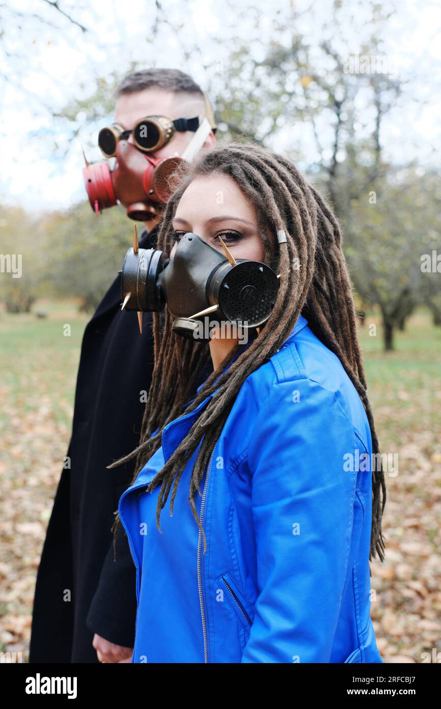 Une femme avec des dreadlocks et un masque à gaz et un homme avec des lunettes steampunk et un masque à gaz posent dans un parc d'automne. Concept de catastrophe écologique. Vertical p Banque D'Images