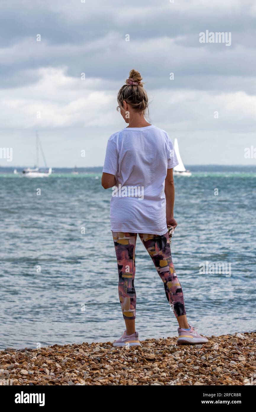 jeune femme portant des leggings floraux debout sur une plage au bord de la mer regardant vers la mer sur une journée ensoleillée. Banque D'Images