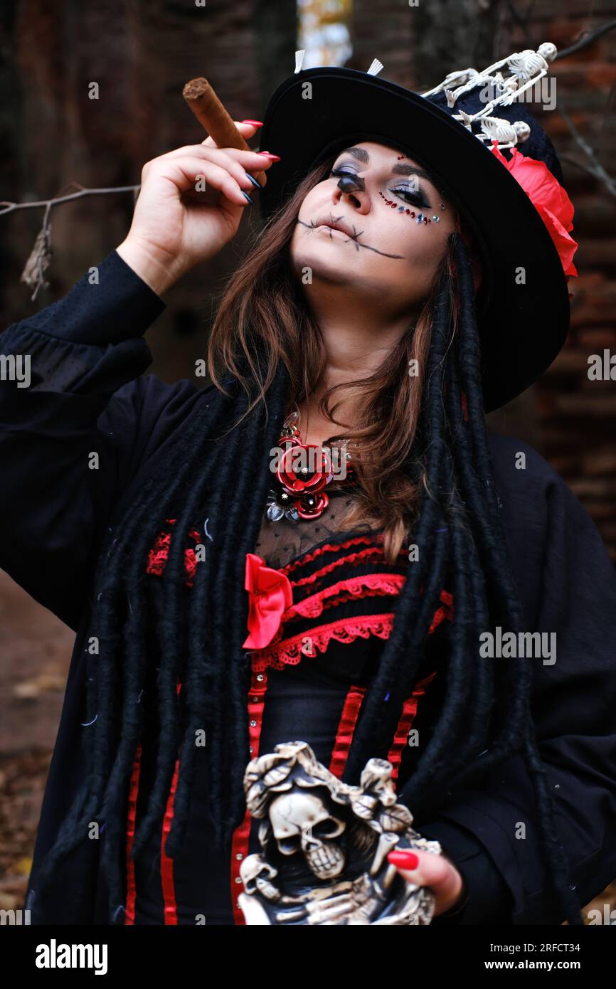 Une femme en forme de Baron Saturday avec un cigare à la main. Le modèle est habillé d'un corset, d'un cardigan et d'un chapeau haut de gamme décoré de figuier squelette Banque D'Images