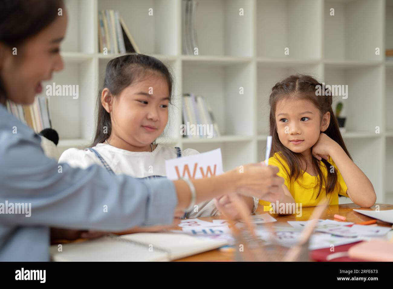 Deux adorables jeunes filles asiatiques se concentrent sur l'étude des cartes-éclair de l'alphabet anglais avec un professeur privé à la maison. préscolaire, maternelle, élémentaire Banque D'Images
