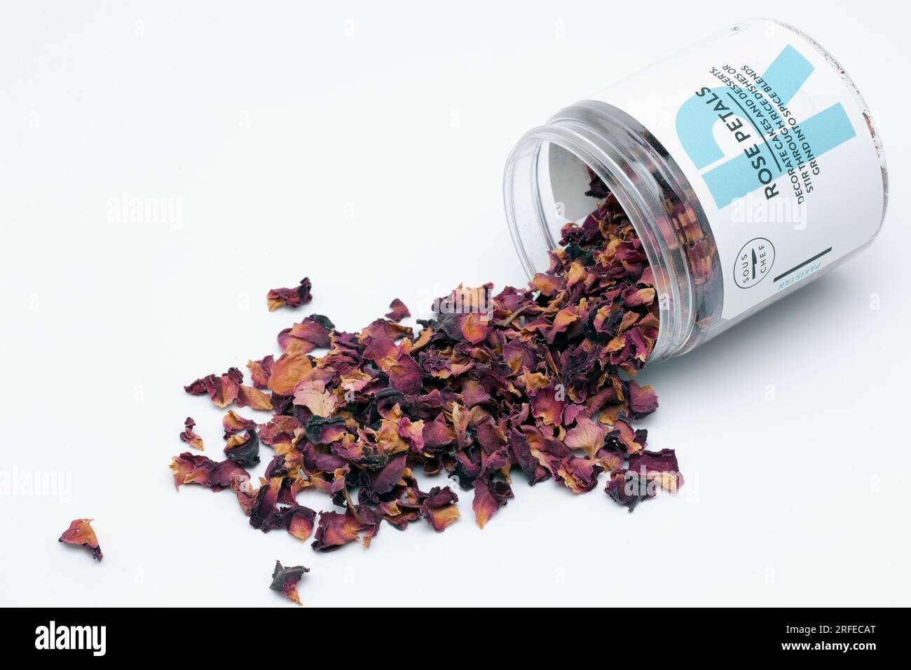 Récipient en plastique de pétales de rose séchés avec le dessus enlevé et renversé sur une surface blanche pour décorer les plats et les desserts Banque D'Images