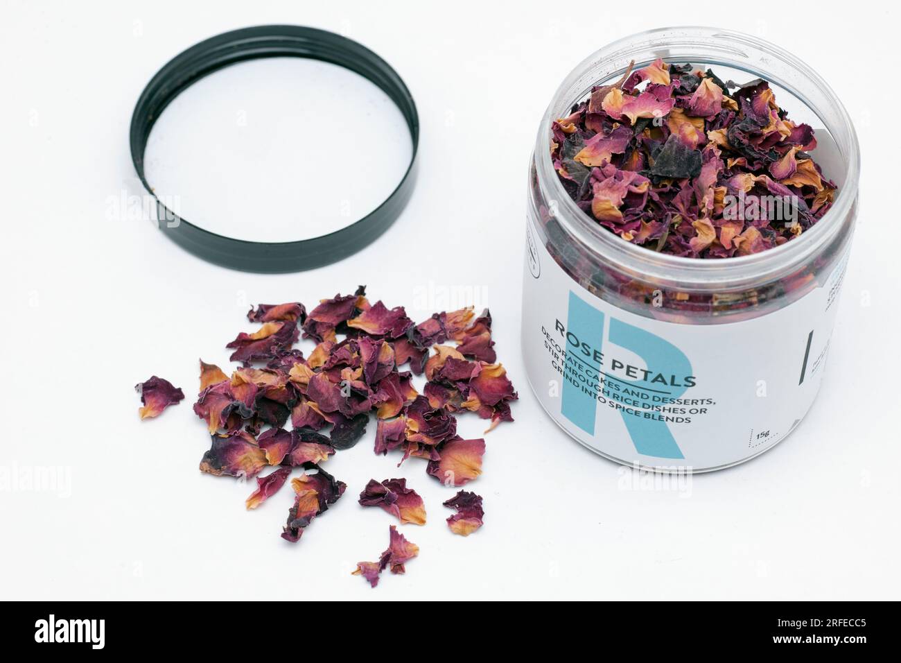 Récipient en plastique de pétales de rose séchés avec le dessus enlevé et renversé sur une surface blanche pour décorer les plats et les desserts Banque D'Images