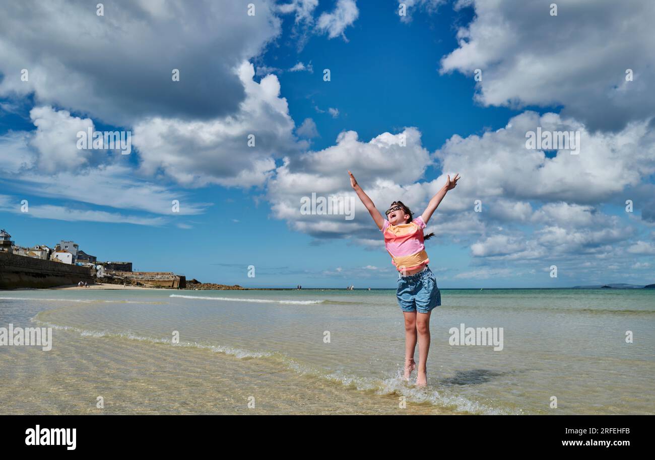 Une jeune fille sautant dans les airs, jouant sur la plage du port de St Ives, Cornwall, Royaume-Uni Banque D'Images