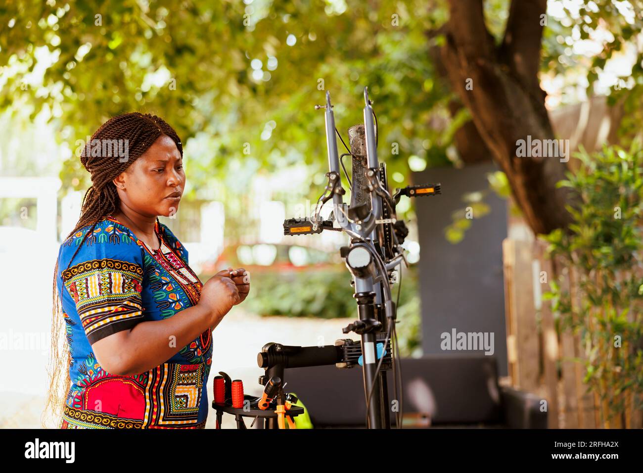 Femme passionnée de sport engagée travaillant à l'extérieur en été sur le vélo moderne. Femme afro-américaine active inspectant minutieusement pour les dommages sur le vélo pour réparer et réparer comme entretien annuel. Banque D'Images