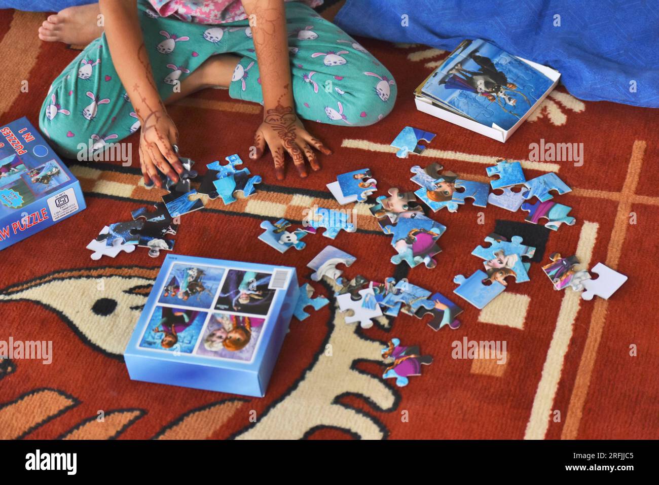 Jeune fille jouant des puzzles et connectant des pièces de puzzle à la maison, ses mains peintes au henné, Pune, Maharashtra, Inde Banque D'Images