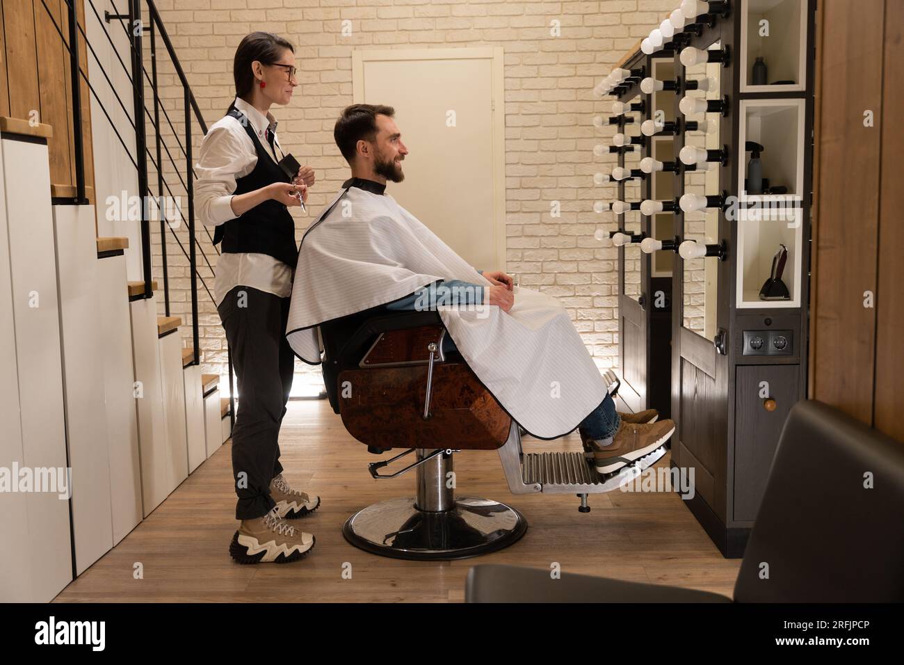 Client satisfait assis dans un salon de coiffure dans une chaise de coiffure, à côté d'un maître avec des ciseaux Banque D'Images