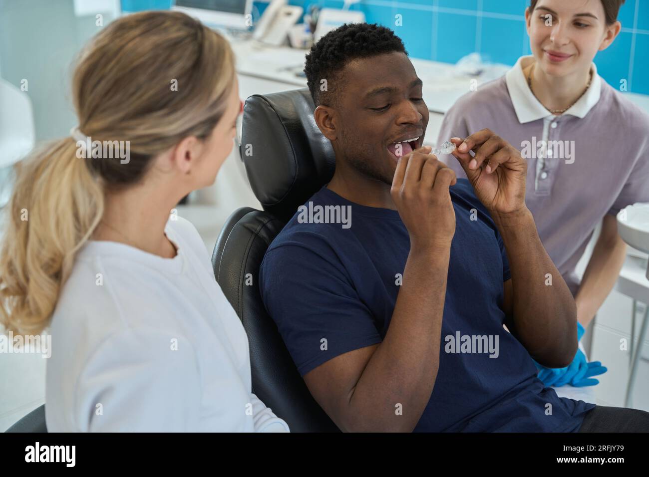 Médecin et infirmière hautement qualifiés surveillant le client masculin qui va mettre des aligneurs transparents à la première fois, redresser les dents, dentisterie esthétique Banque D'Images